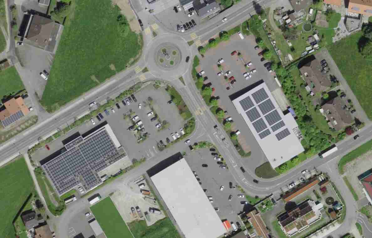 Orthofoto von Gretzenbach an der Oltnerstrasse im Grund mit Kreisel als zentralem Verkehrsknoten, von dem mehrere Strassen abzweigen. Rundherum liegen Gewerbebauten mit Photovoltaik-Dächern, dazugehörige Parkplätze mit zahlreichen Fahrzeugen sowie Wohnhäuser mit Gärten. Fussgängerstreifen queren die Zufahrten zum Kreisel. Die Strassen sind zwei- bis mehrspurig ausgebaut und ermöglichen sowohl motorisierten Verkehr als auch Fussgängerquerungen.