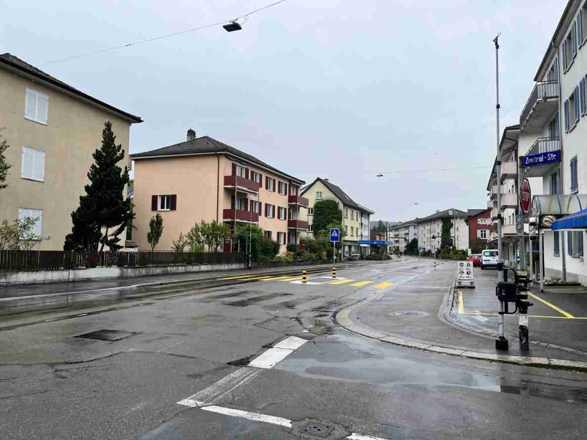 Kreuzungsbereich Schaffhauserstrasse/Zentral-Strasse mit nasser Fahrbahn nach Niederschlag. Strassenschild «Zentral-Str.» sowie ein Stoppschild markieren die Nebenstrasse als untergeordnet gegenüber der durchgehenden Hauptstrasse. Eine Mittelinsel mit Fussgängerstreifen und Vorwarntafel dient der Querung. Am rechten Bildrand ist ein Messgerät zur Verkehrszählung an einem Mast montiert. Wenig Verkehr, im Hintergrund ein Fahrrad und parkierte Autos.